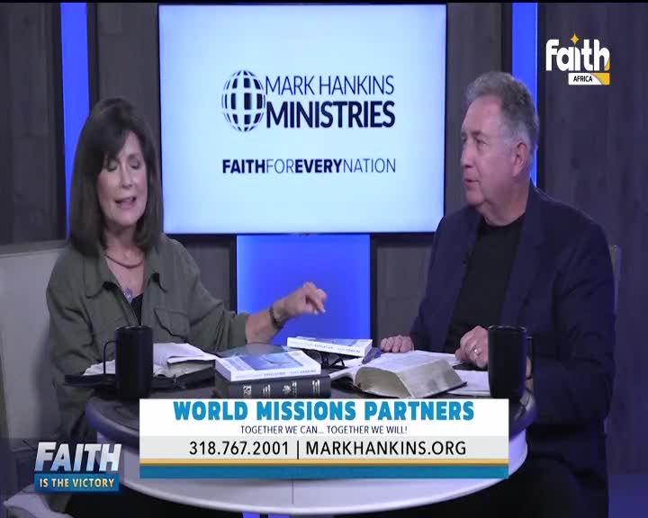 On the set of Faith TV in South Africa, a man and woman sit at a small table, gesturing as they speak. Books and mugs are scattered around them, and a large screen displays the Mark Hankins Ministries logo.
