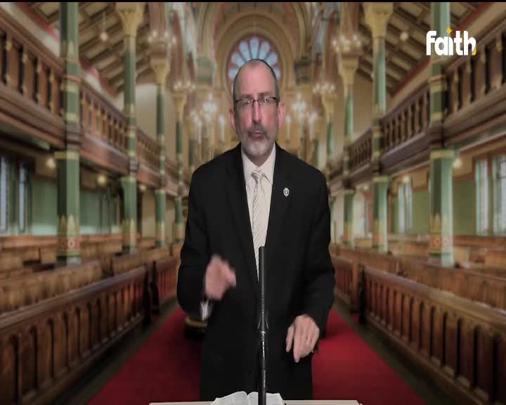 A man in a suit gestures with his hands, speaking into a microphone. Behind him, the backdrop depicts rows of pews in a large, ornate hall, and the Faith TV logo is visible in the corner.
