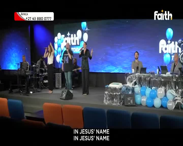 Three singers on stage, arms raised, are belting out a song. The backdrop features the Faith TV logo, and the words "In Jesus' Name" scroll across the bottom.
