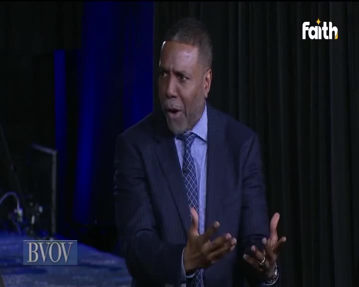 The man in the suit gestures with both hands, his expression open-mouthed. A Faith TV logo sits in the corner, and the backdrop is a simple curtain.
