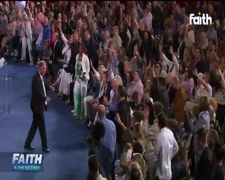 A man in a dark suit walks forward on a blue carpet, while the crowd around him raises their hands. The "Faith TV" logo is visible in the corner.
