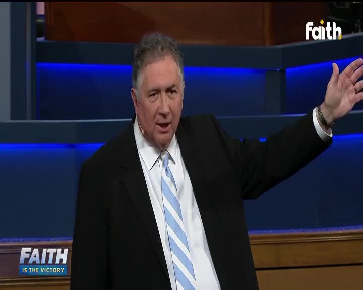 A man in a suit gestures emphatically, his right arm extended. He's on a Faith TV set, speaking with conviction.

