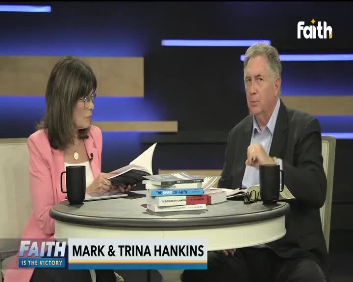 Mark and Trina Hankins are seated at a table, discussing something on Faith TV. Trina reads from a book, while Mark gestures with his hand as he speaks.
