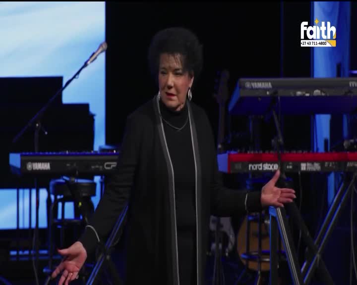A woman with dark, permed hair gestures with her hands as she speaks on a stage. Behind her, a Yamaha keyboard and a red Nord Stage keyboard sit ready. The Faith TV logo is visible in the upper right corner.