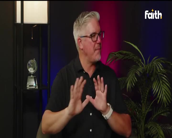 A man with glasses gestures with his hands on a Faith TV broadcast. His expression is earnest as he speaks, with a lush plant and a globe on a shelf behind him.