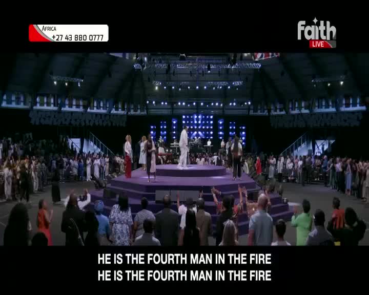 A man in a white suit stands on a raised platform, surrounded by people in the audience. The Faith TV broadcast shows a large congregation gathered in a stadium. A man in a white suit stands on a raised platform, surrounded by people in the audience. The Faith TV broadcast shows a large congregation gathered in a stadium.