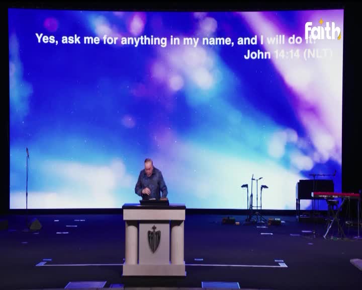A man stands at a pulpit, gesturing as he speaks to the congregation. The Faith TV logo is visible on the large screen behind him, displaying scripture from John 14:14. A man stands at a pulpit, gesturing as he speaks to the congregation. The Faith TV logo is visible on the large screen behind him, displaying scripture from John 14:14.
