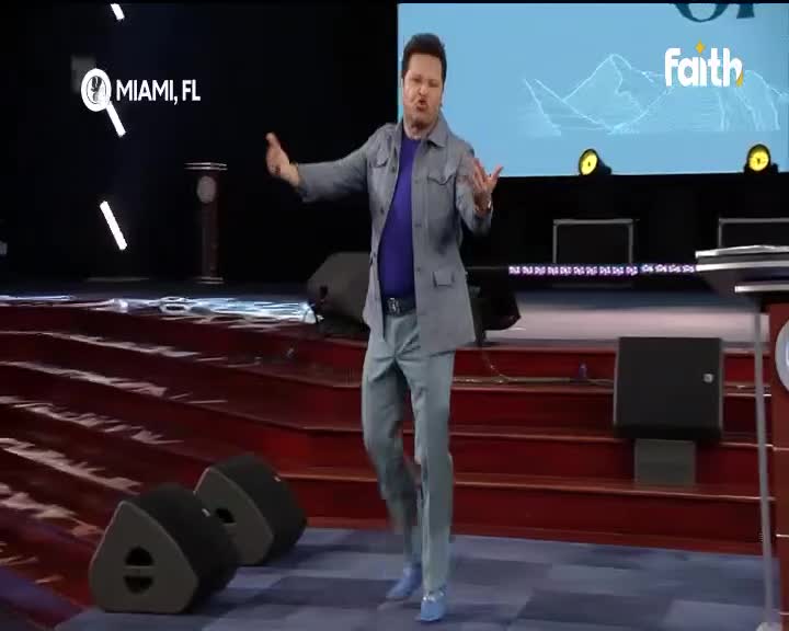 A man in a light grey jacket and blue shirt gestures with both hands as he speaks on a stage. The Faith TV logo appears on a screen behind him, with "Miami, FL" displayed on the left. A man in a light grey jacket and blue shirt gestures with both hands as he speaks on a stage. The Faith TV logo appears on a screen behind him, with "Miami, FL" displayed on the left.