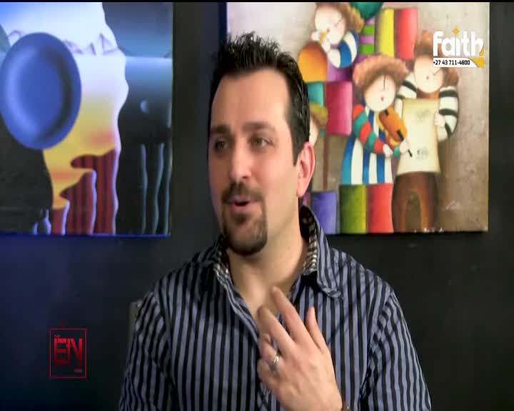 A man with a goatee, wearing a striped shirt, speaks with his hand raised to his chest. Behind him, a colorful painting of children with musical instruments hangs on the wall, with a Faith TV logo in the corner.