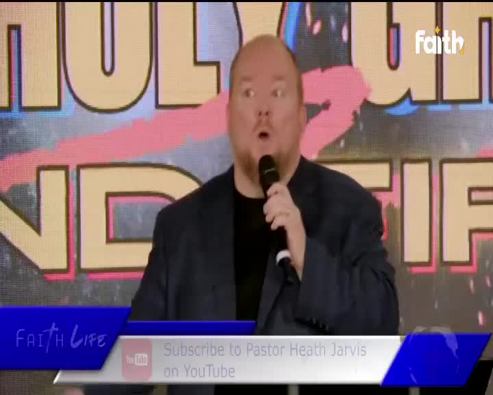 A man with a surprised expression speaks into a microphone, his dark suit jacket open. Behind him, large yellow letters spell out part of a message on a screen, with the Faith TV logo visible in the upper right corner.