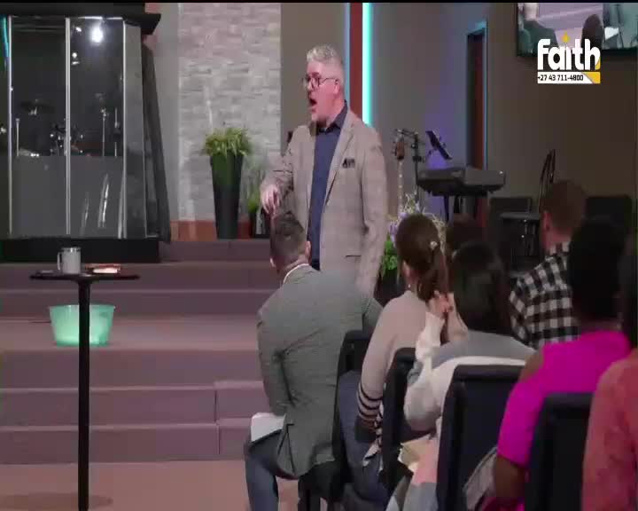 A man in a suit jacket gestures emphatically from a raised platform, addressing a seated congregation. The Faith TV logo is visible on a screen behind him.