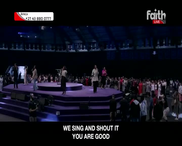 A group of singers stands on a raised, purple stage, facing a large congregation. Cameras are positioned in front of the stage, capturing the performance for Faith TV.
