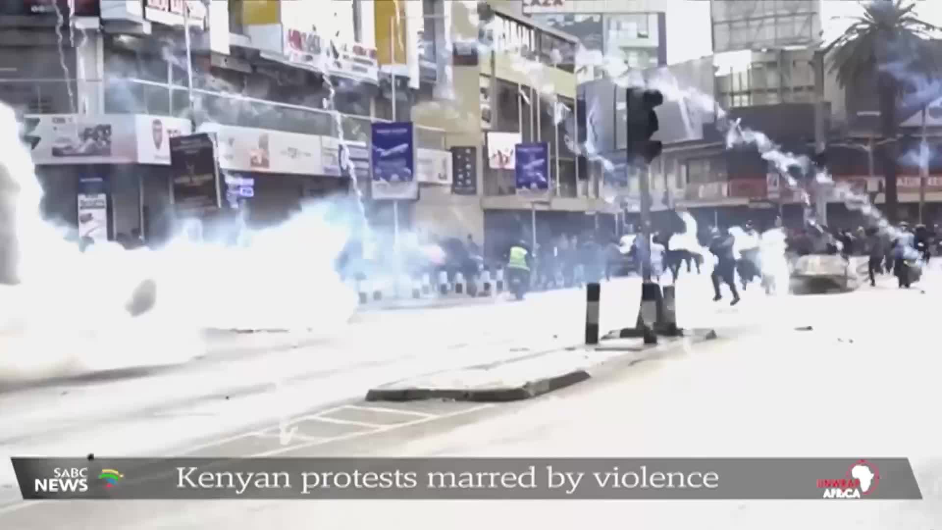 White smoke billows across the street, obscuring the view as people run from the right side of the frame. The SABC News report from South Africa shows the aftermath of a protest in Kenya.

