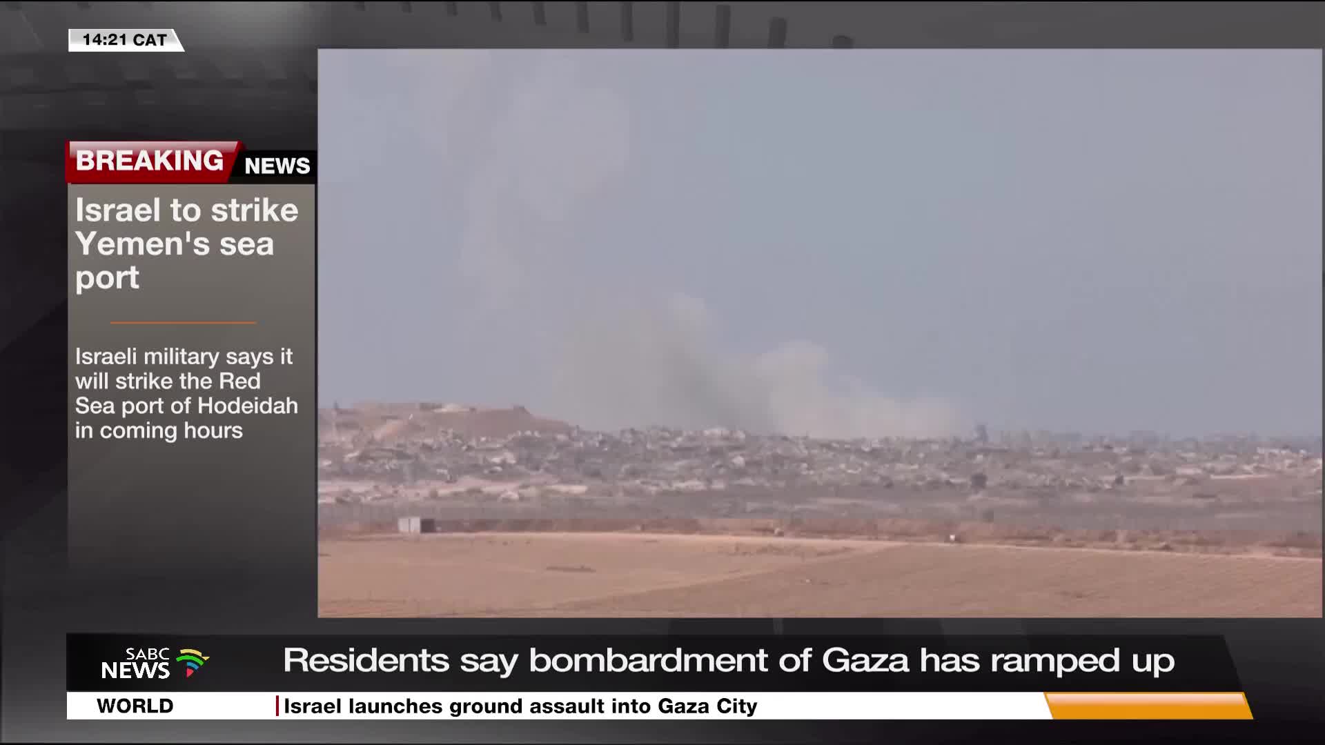 A plume of smoke rises over a distant town, as reported by SABC News. The breaking news banner warns of an impending strike on a Yemeni port.

