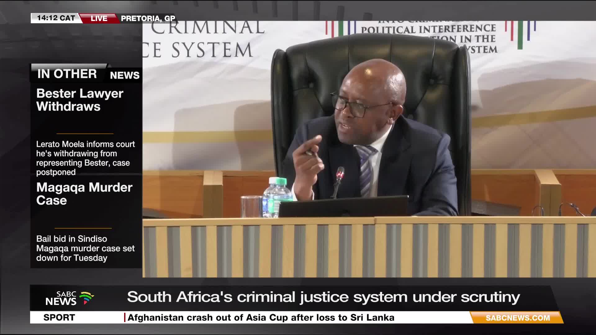 A man in a suit gestures emphatically while speaking, his voice amplified by a microphone. SABC News is reporting live from Pretoria, where South Africa's criminal justice system is under scrutiny.
