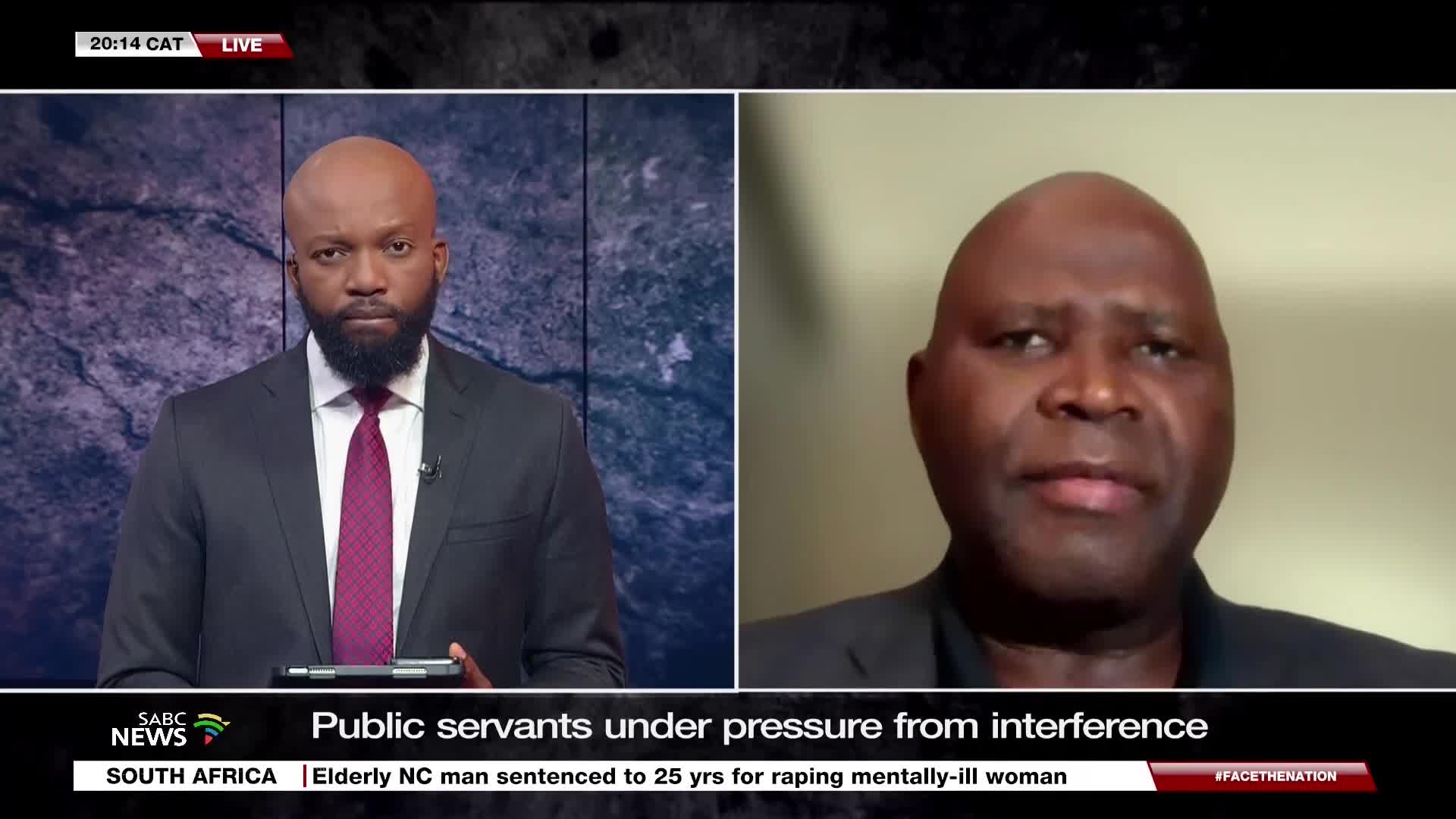 An SABC News anchor, wearing a dark suit and a burgundy tie, is facing the camera. On the right, a man is speaking, presumably as part of a live interview.
