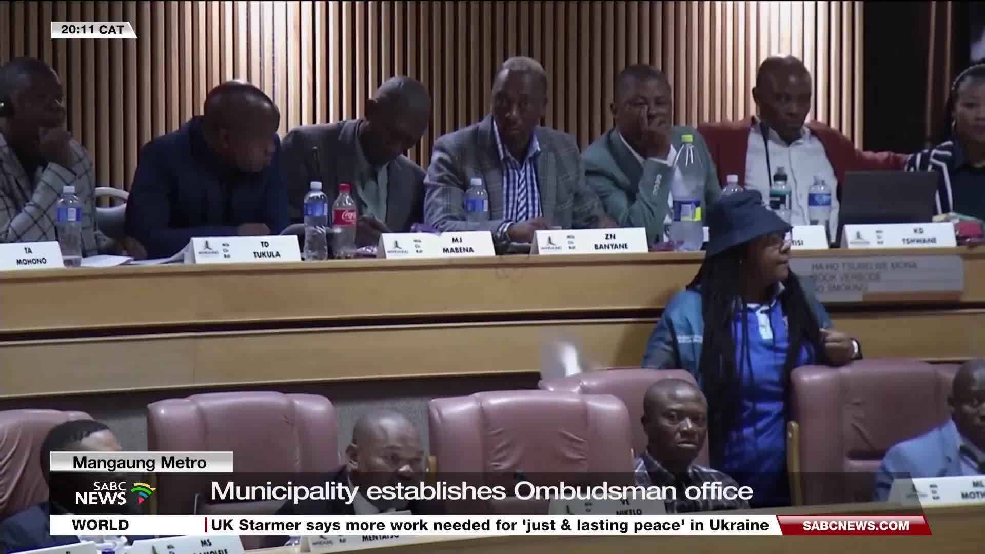 A panel of people sits at a table, some with their heads down, as a person with dreadlocks and a blue bucket hat gestures while speaking. The SABC News graphic at the bottom reports on the Mangaung Metro.
A panel of people sits at a table, some with their heads down, as a person with dreadlocks and a blue bucket hat gestures while speaking. The SABC News graphic at the bottom reports on the Mangaung Metro.