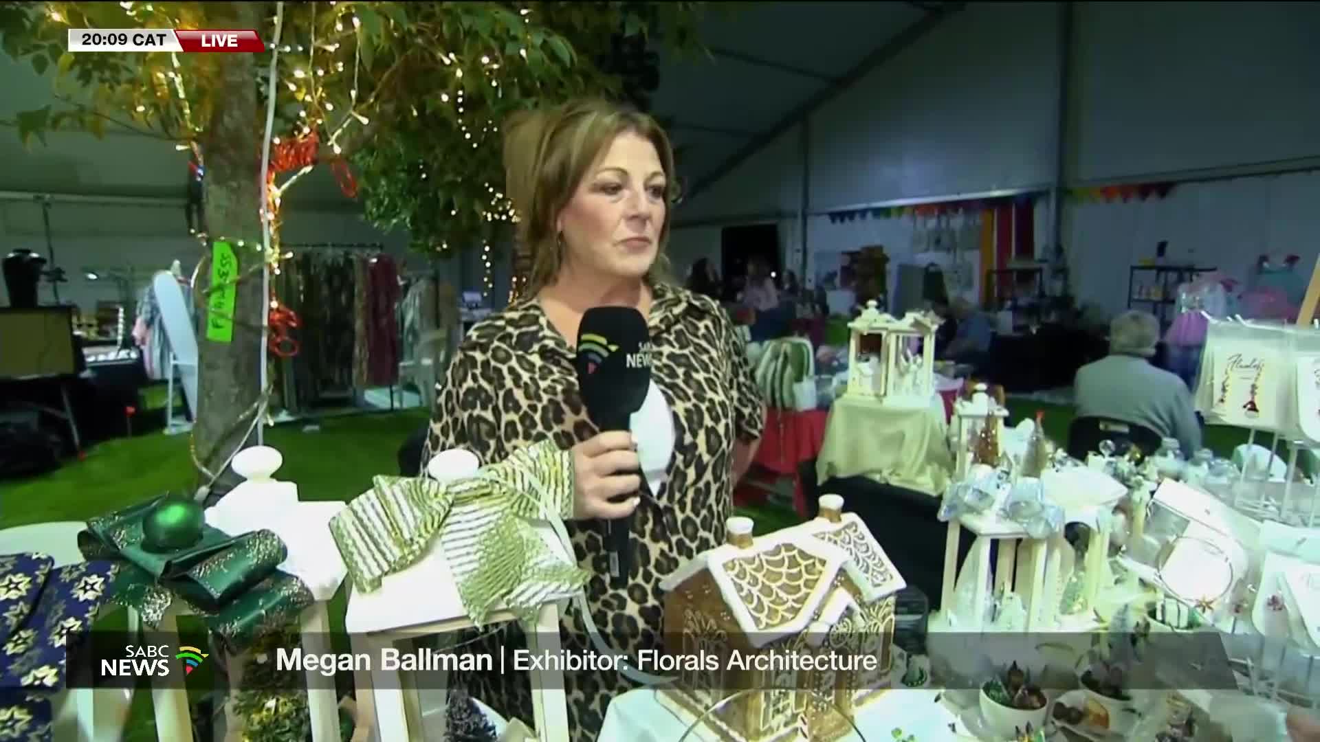 An SABC News reporter, microphone in hand, is speaking live from an outdoor market in South Africa. Behind her, tables are laden with crafts and decorative items, illuminated by the warm glow of string lights.
An SABC News reporter, microphone in hand, is speaking live from an outdoor market in South Africa. Behind her, tables are laden with crafts and decorative items, illuminated by the warm glow of string lights.