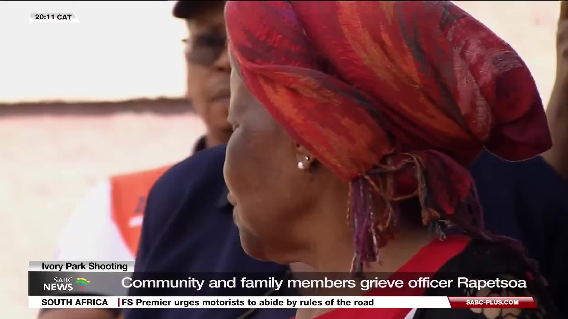 A woman in a vibrant red headscarf, her face turned away, stands with others. The SABC News graphic at the bottom of the screen indicates the community is grieving the loss of Officer Rapetsoa.
A woman in a vibrant red headscarf, her face turned away, stands with others. The SABC News graphic at the bottom of the screen indicates the community is grieving the loss of Officer Rapetsoa.