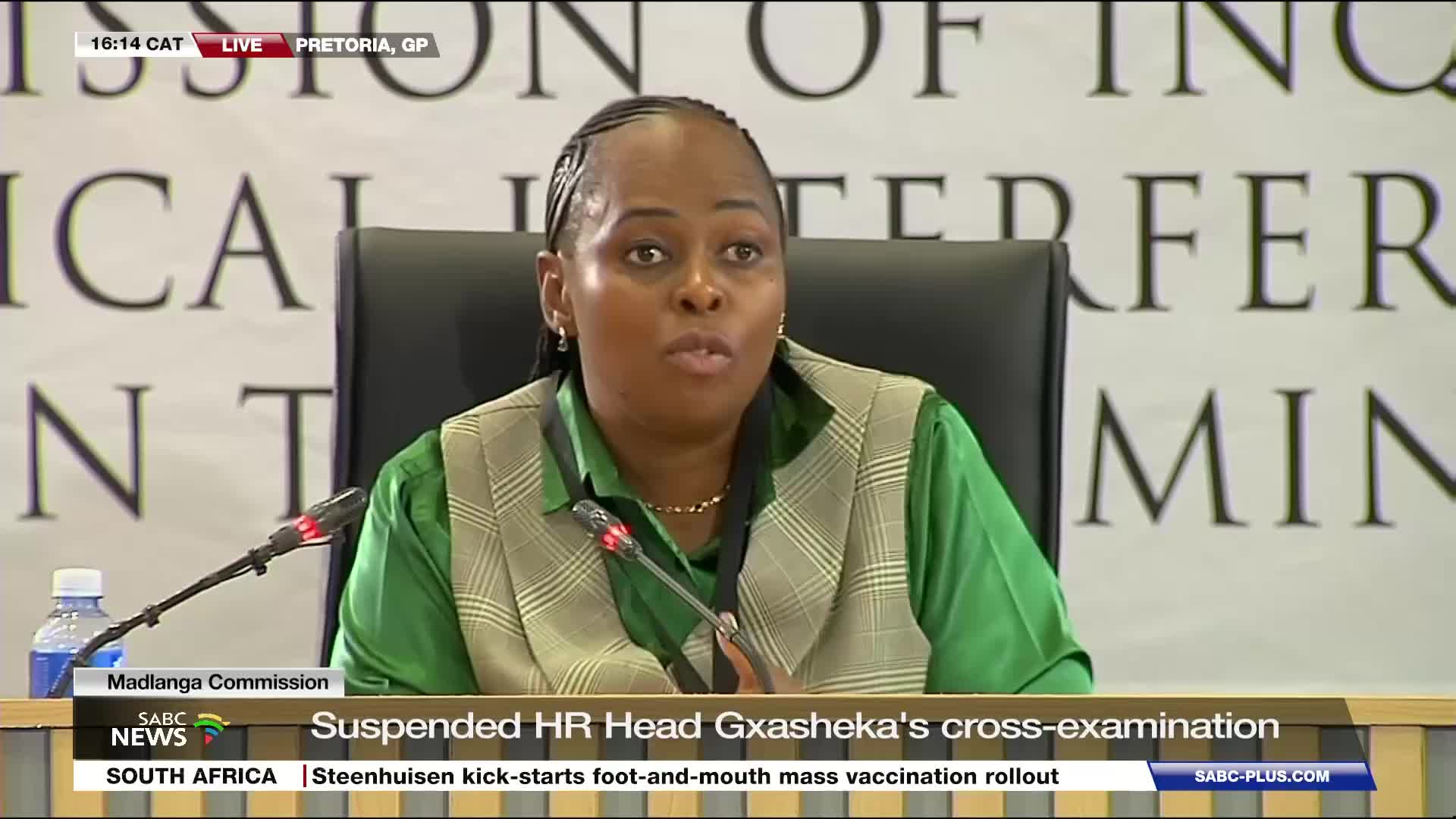 A woman in a green shirt and patterned vest speaks into a microphone at a commission hearing. SABC News is covering the cross-examination of a suspended HR head in Pretoria. A woman in a green shirt and patterned vest speaks into a microphone at a commission hearing. SABC News is covering the cross-examination of a suspended HR head in Pretoria.