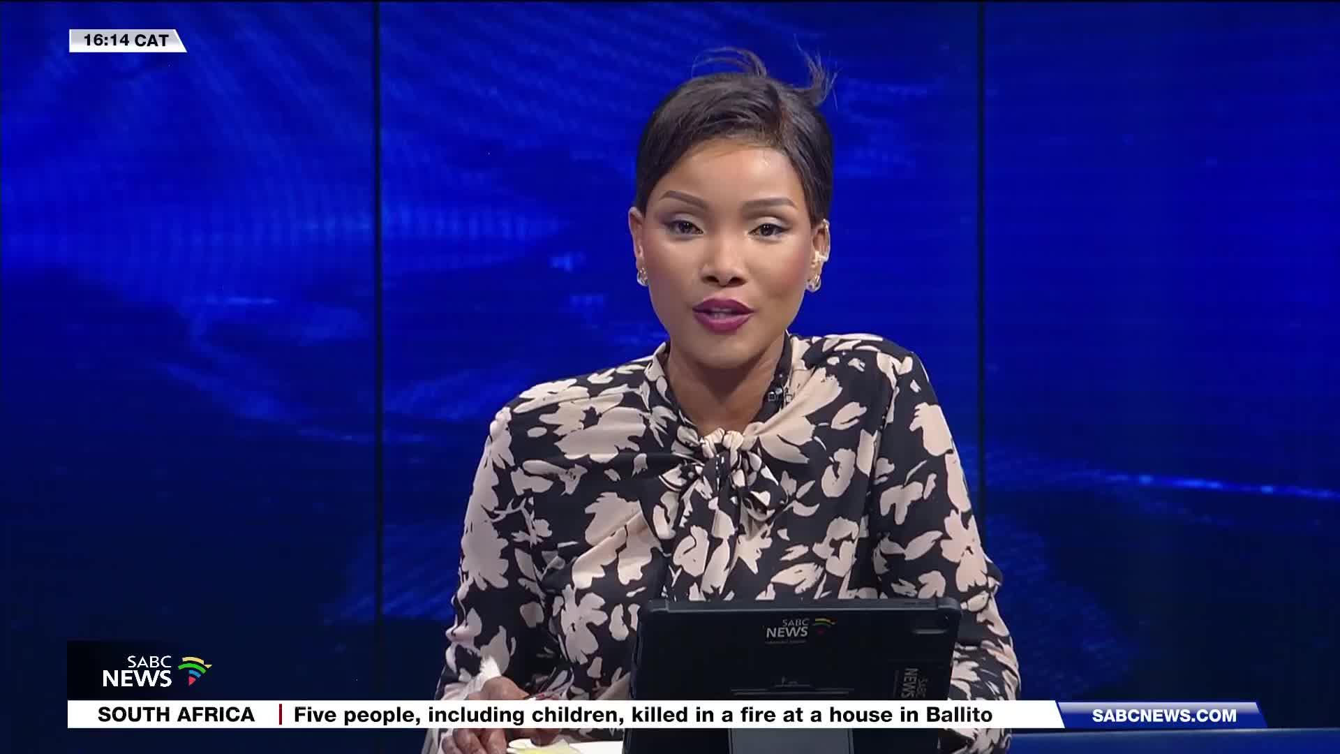 The SABC News anchor is speaking into the camera, her patterned blouse a stark contrast to the deep blue backdrop. A chyron at the bottom of the screen reports a tragic fire in Ballito. The SABC News anchor is speaking into the camera, her patterned blouse a stark contrast to the deep blue backdrop. A chyron at the bottom of the screen reports a tragic fire in Ballito.