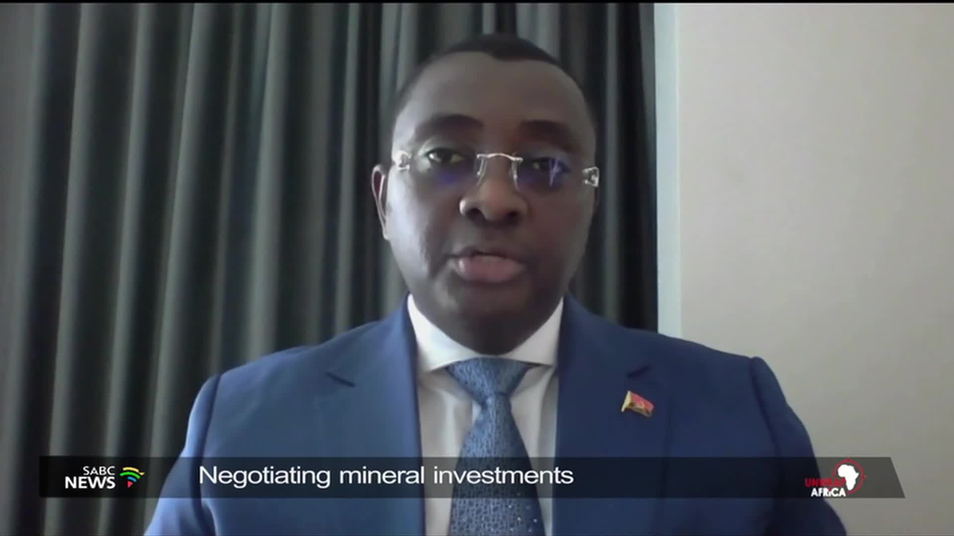 A man in a blue suit and tie speaks directly to the camera, his glasses reflecting the light. A SABC News graphic indicates he is discussing mineral investments in Africa. A man in a blue suit and tie speaks directly to the camera, his glasses reflecting the light. A SABC News graphic indicates he is discussing mineral investments in Africa.