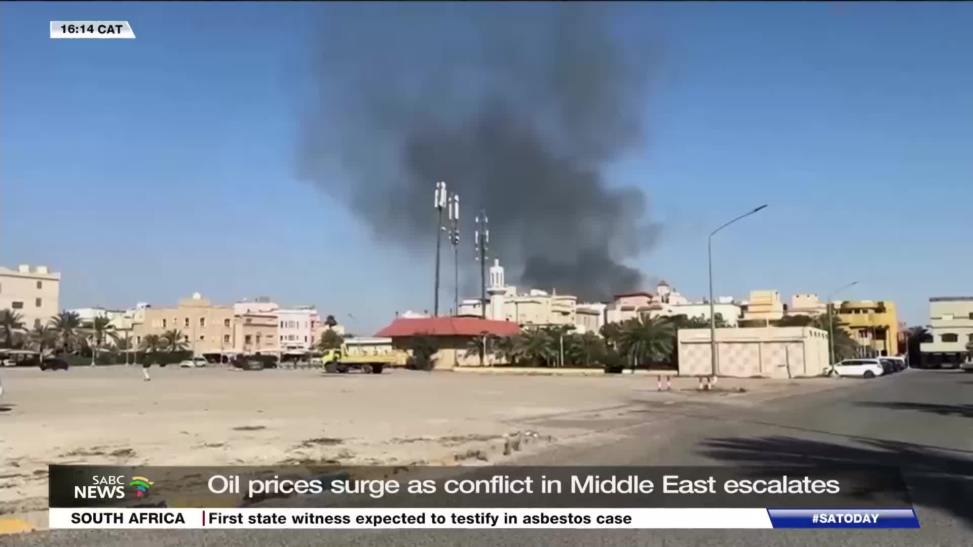Thick black smoke billows into the clear blue sky from a cluster of buildings. A yellow truck sits parked on the dusty ground in front of the scene, its presence stark against the backdrop of the SABC News report about escalating conflict. Thick black smoke billows into the clear blue sky from a cluster of buildings. A yellow truck sits parked on the dusty ground in front of the scene, its presence stark against the backdrop of the SABC News report about escalating conflict.