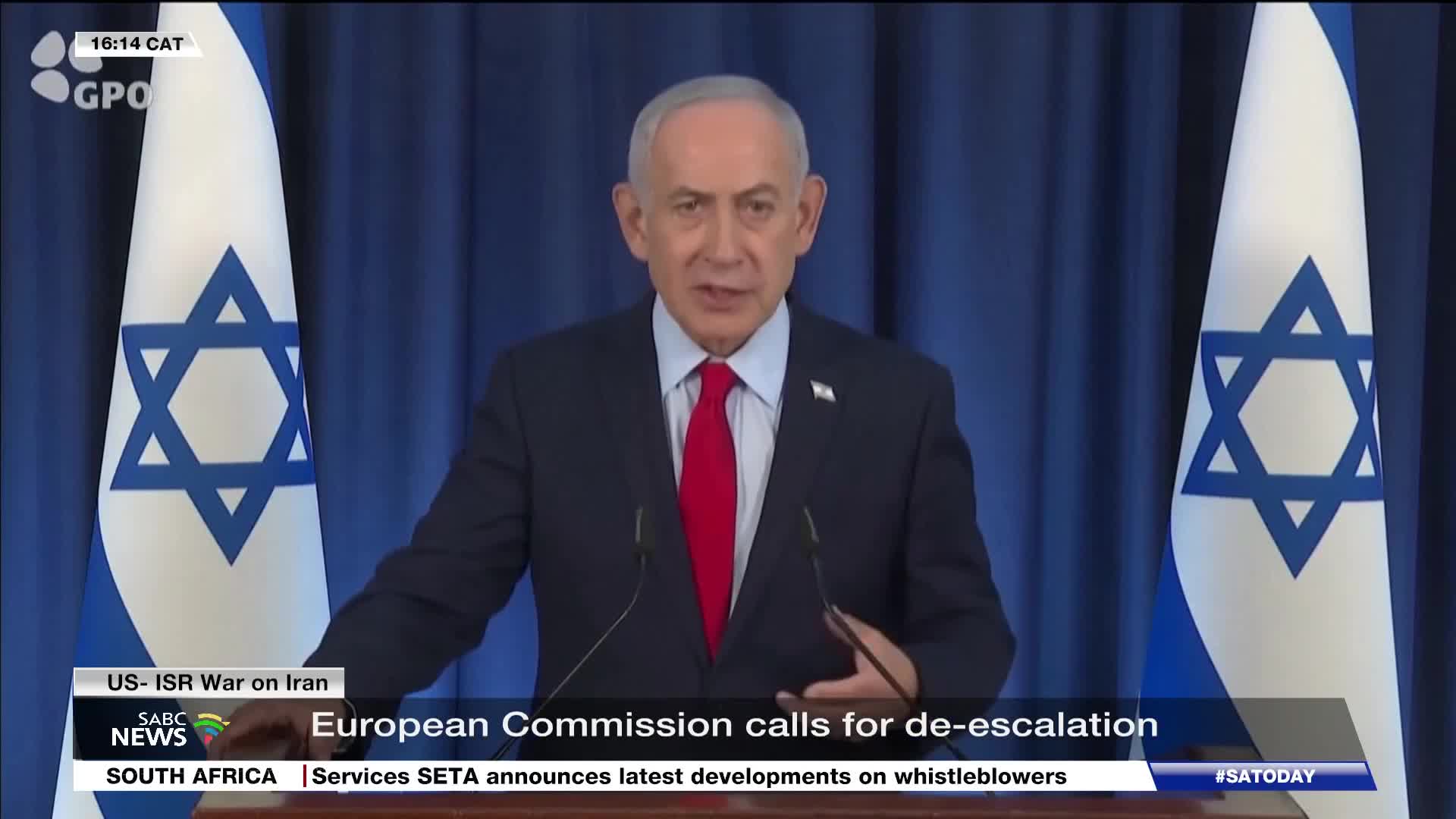 The man in the dark suit and red tie speaks at a podium, flanked by Israeli flags. A news ticker from SABC News scrolls across the bottom of the screen.