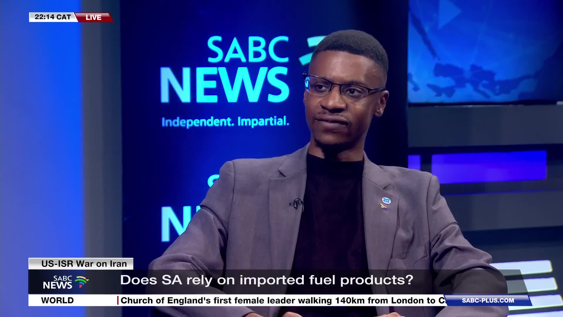 A man in a grey suit jacket sits in front of a SABC News backdrop, his gaze directed slightly off-camera. A lower-third graphic asks, "Does SA rely on imported fuel products?"