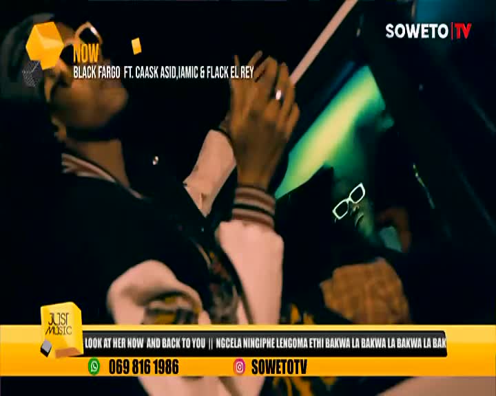 A man in a black jacket and cap raises his hands, while another person wearing white-framed sunglasses is in the background. The music video is playing on Soweto TV, with the song title and artist names displayed at the top.
