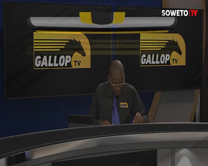 A man in a gray shirt and glasses is seated behind a desk, papers in front of him. The Soweto TV logo and "Gallop TV" are visible on the screen behind him.
