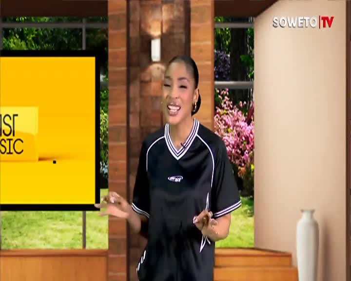 The Soweto TV presenter gestures with her hands, smiling as she speaks. A bright yellow screen displaying "IST MUSIC" sits to her left.
