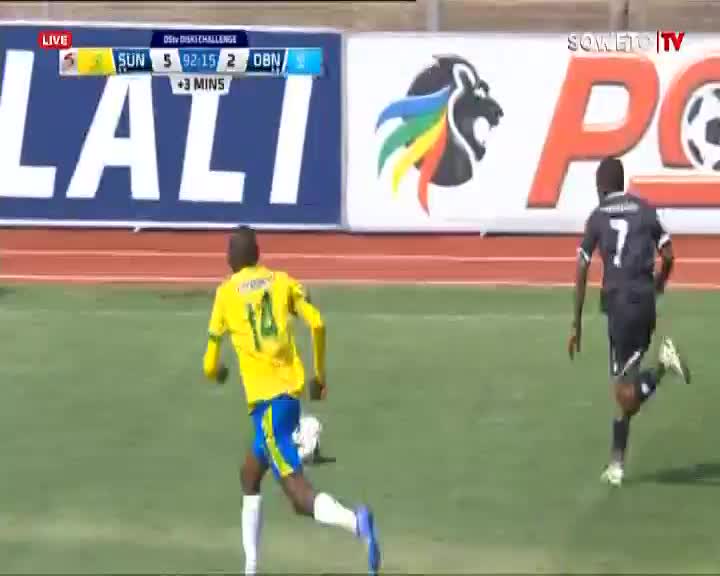 The player in yellow sprints toward the ball, his blue shorts and socks bright against the green pitch. Number 7 in black chases him, the score on Soweto TV showing the home team is winning.
