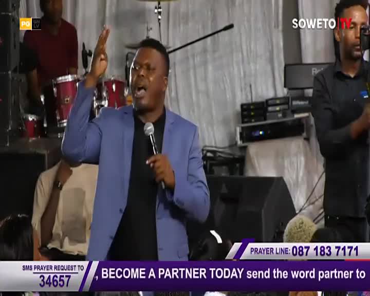 A man in a blue blazer speaks passionately into a microphone, his right hand raised. Soweto TV's logo is visible, and calls for prayer and partnership are displayed on the screen.
