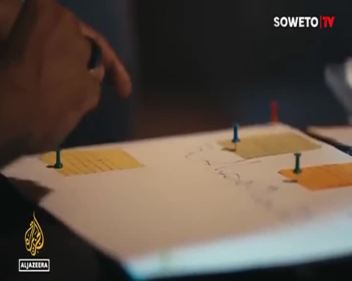 A hand points at a map on a table, with colorful pins marking locations. This is part of a Soweto TV broadcast, likely discussing local South African events. A hand points at a map on a table, with colorful pins marking locations. This is part of a Soweto TV broadcast, likely discussing local South African events.