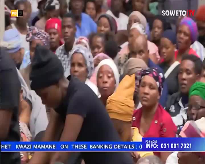 A young person in a black beanie bends down, their face obscured. A crowd of people, many wearing headscarves, watches intently. A young person in a black beanie bends down, their face obscured. A crowd of people, many wearing headscarves, watches intently.