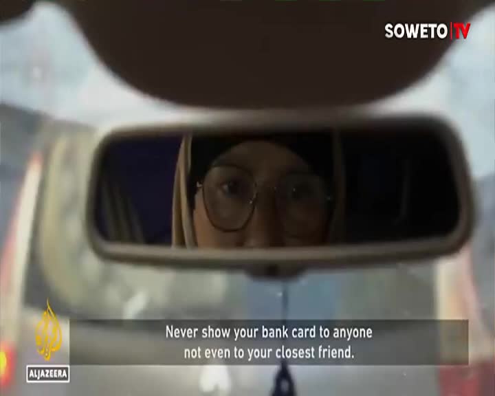 A woman's face, framed by glasses and a headscarf, stares back from the rearview mirror. The Soweto TV logo is visible in the corner, alongside a warning about bank card security.