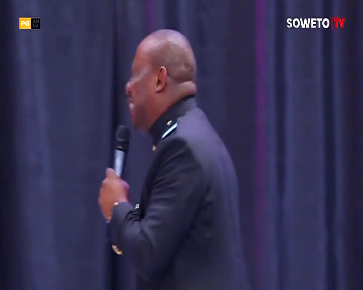 A man in a dark suit speaks into a microphone, his head turned to the side. The Soweto TV logo appears in the top right corner.