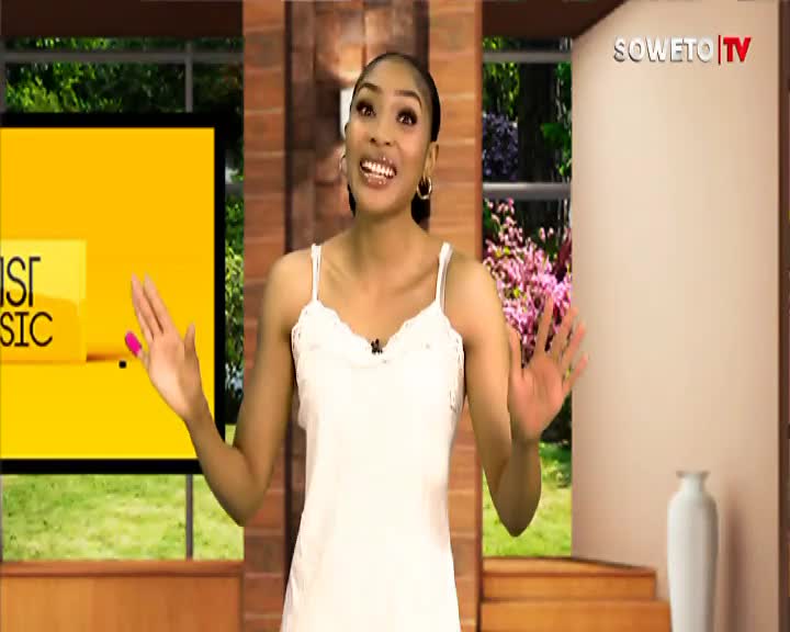 A woman in a white slip dress gestures with both hands, her bright pink nail polish catching the light. The Soweto TV logo is visible in the upper right corner, beside a backdrop of blooming pink flowers. A woman in a white slip dress gestures with both hands, her bright pink nail polish catching the light. The Soweto TV logo is visible in the upper right corner, beside a backdrop of blooming pink flowers.
