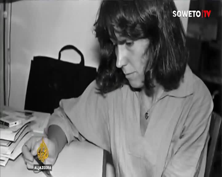 A woman with dark, wavy hair looks down at papers on a desk. A Soweto TV logo appears in the upper right corner. A woman with dark, wavy hair looks down at papers on a desk. A Soweto TV logo appears in the upper right corner.