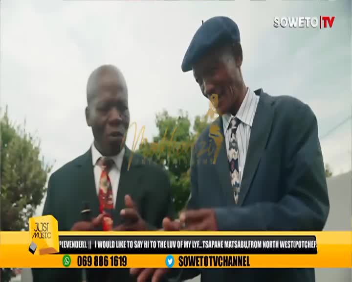 Two men in suits stand talking, one wearing a flat cap. A Soweto TV graphic overlays the scene. Two men in suits stand talking, one wearing a flat cap. A Soweto TV graphic overlays the scene.