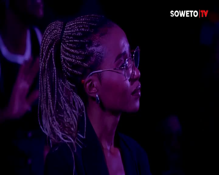 The woman's braided hair swings slightly as she turns her head. A Soweto TV logo appears in the corner of the frame.