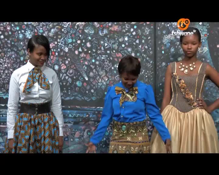 On the Tshwane TV set, three women stand in front of a colorful backdrop, each modeling a different outfit with bold patterns. The woman in the center gestures with her hands, while the others pose with a serious expression.
