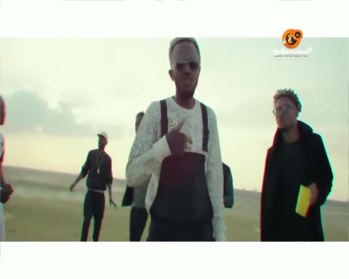 The main guy in the middle is pointing his finger, while others stand around him in a wide, open space. The scene looks like it's from a music video, maybe something playing on Tshwane TV.
