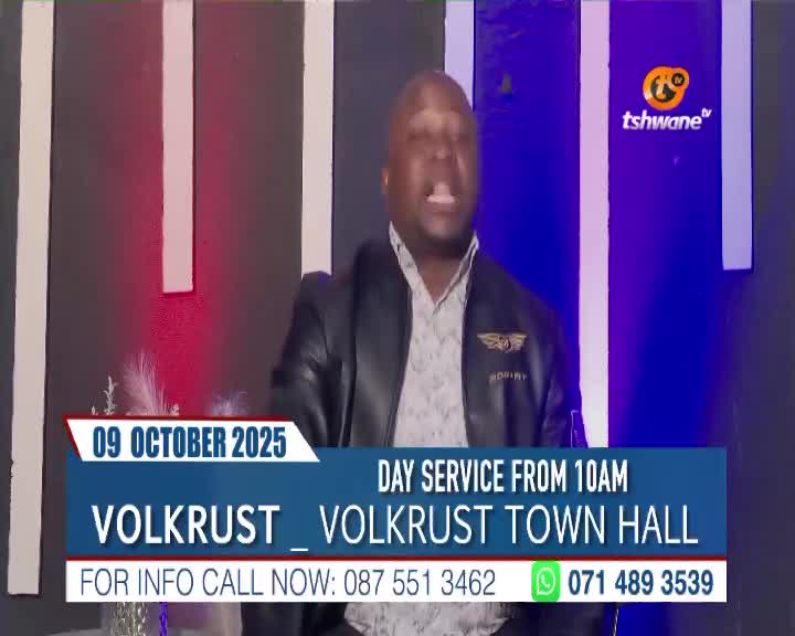 A man in a black jacket gestures emphatically, speaking directly to the camera on Tshwane TV. The screen displays information about a day service in Volkrust, South Africa.
