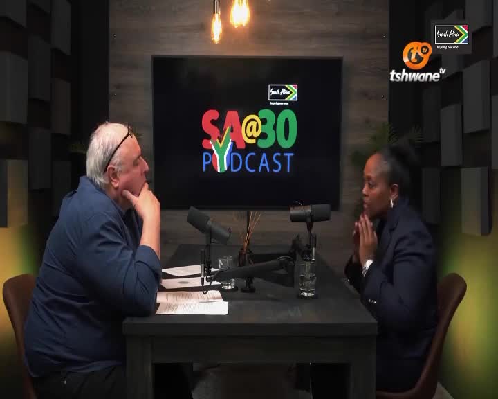 Two people are seated at a table with microphones, the man leaning forward with his hand to his chin, the woman with her hands clasped. The backdrop declares "SA@30 Podcast" and the Tshwane TV logo is visible.
