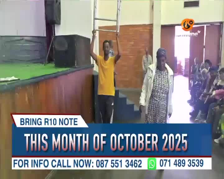A man in a yellow shirt holds a small ladder above his head as he walks toward the camera. A woman in a patterned dress and white jacket walks in the opposite direction, past a seated audience, all under the Tshwane TV logo.
