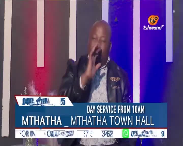 A man in a leather jacket is speaking into a microphone, gesturing with his right hand. The Tshwane TV logo is visible, and the screen displays information about a day service from Mthatha Town Hall.
