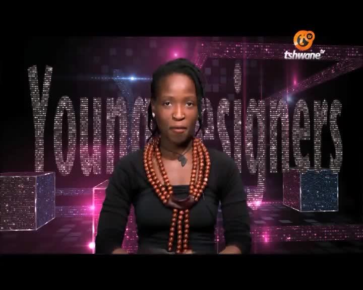 A woman in a black top and beaded necklace speaks directly to the camera, the "Young Designers" logo sparkling behind her on the Tshwane TV set. The background is a dark stage with a futuristic design.
A woman in a black top and beaded necklace speaks directly to the camera, the "Young Designers" logo sparkling behind her on the Tshwane TV set. The background is a dark stage with a futuristic design.