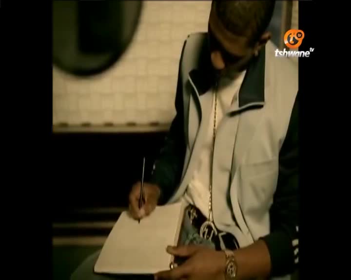 A young man in a tracksuit jacket, a gold chain, and a watch writes on a piece of paper. The Tshwane TV logo appears in the corner of the frame.